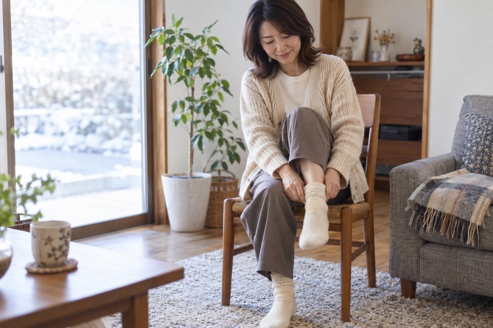 椅子に座り、足元に柔らかな靴下を履く女性