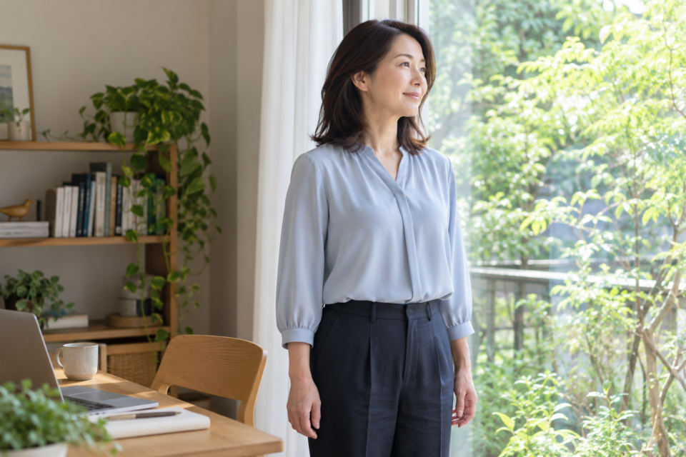 机の作業を中断して窓辺で休憩する女性