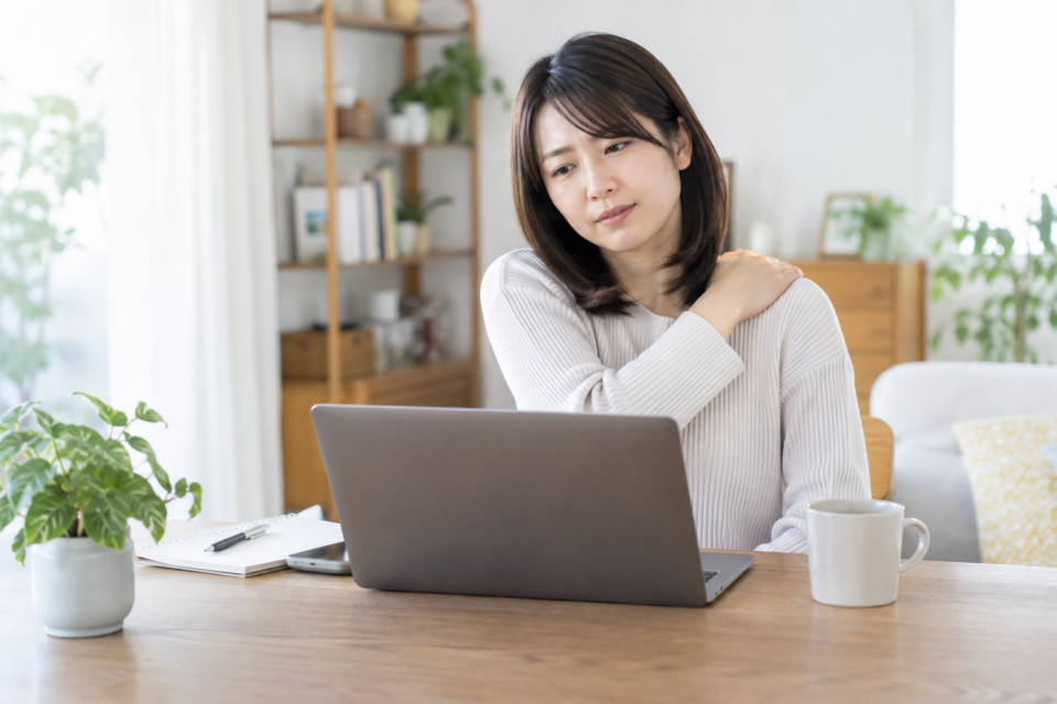 パソコン作業を中断し片側の肩に手を添える女性