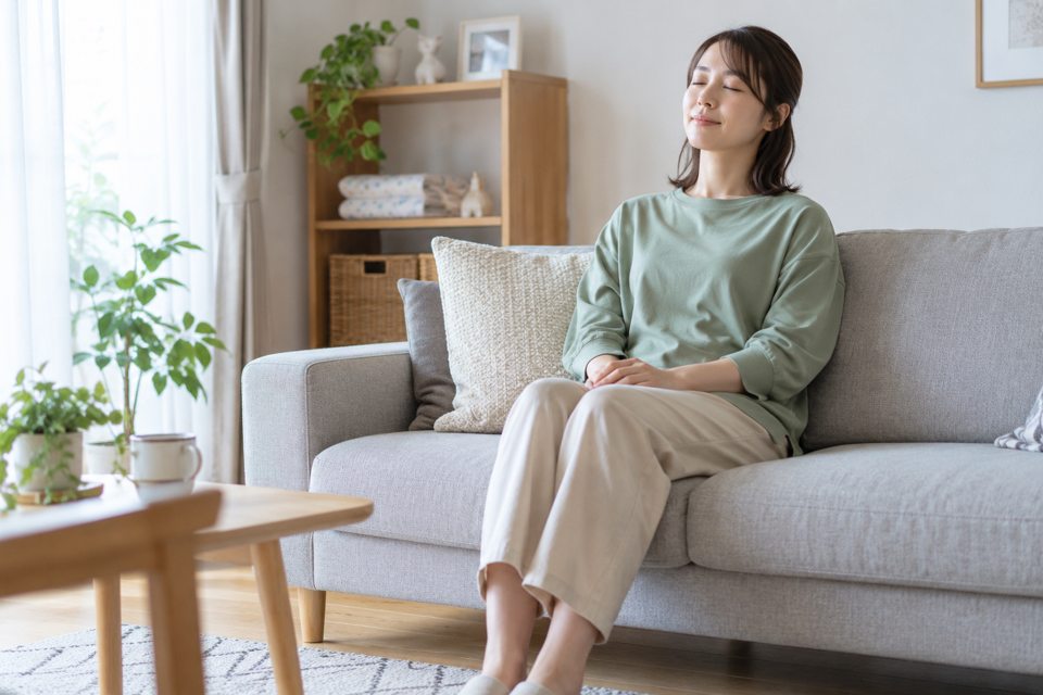 明るい部屋のソファに座り、目を閉じてひと休みする女性